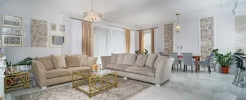 Wnętrze salonu w stylu glamour i quiet luxury z beżową sofą i złotymi akcentami.