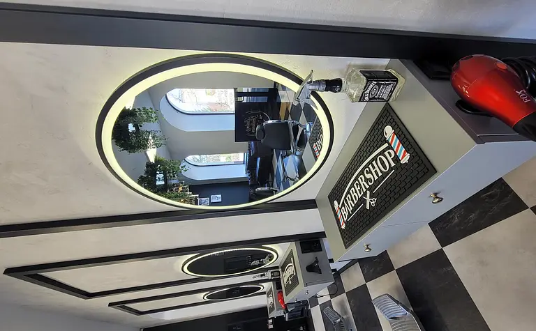 Wnętrze barber shopu z lustrami, roślinami i nowoczesnym wyposażeniem.