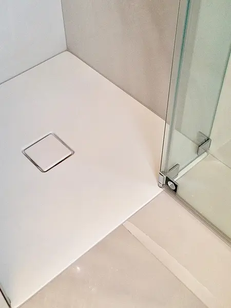 Minimalistyczna łazienka z białą kabiną prysznicową, nowoczesne kafelki, przeszklona przestrzeń.