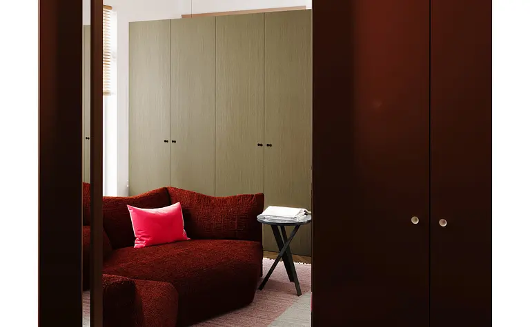 Garderoba w stylu eklektycznym z czerwoną kanapą i zielonymi szafkami, minimalistyczne detale.