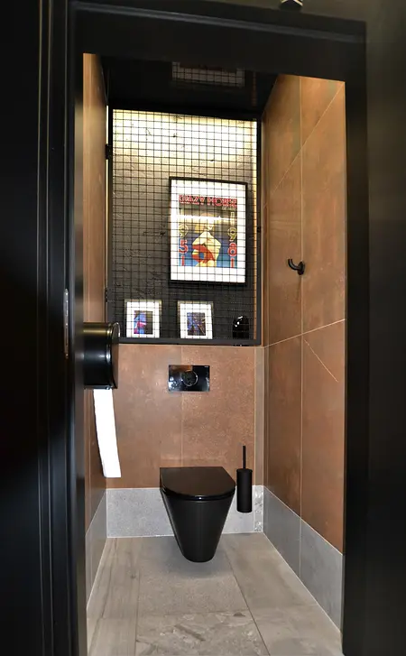Toaleta z brązowymi płytkami, czarnym WC i nowoczesnymi detalami