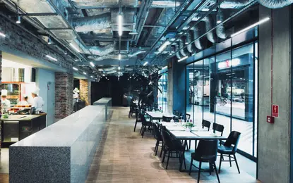 Wnętrze restauracji z industrialnym sufitem, minimalistycznym barem i skandynawskimi krzesłami.