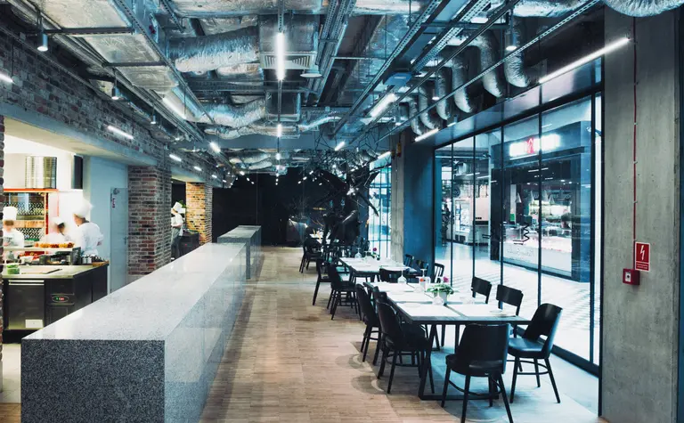 Wnętrze restauracji z industrialnym sufitem, minimalistycznym barem i skandynawskimi krzesłami.