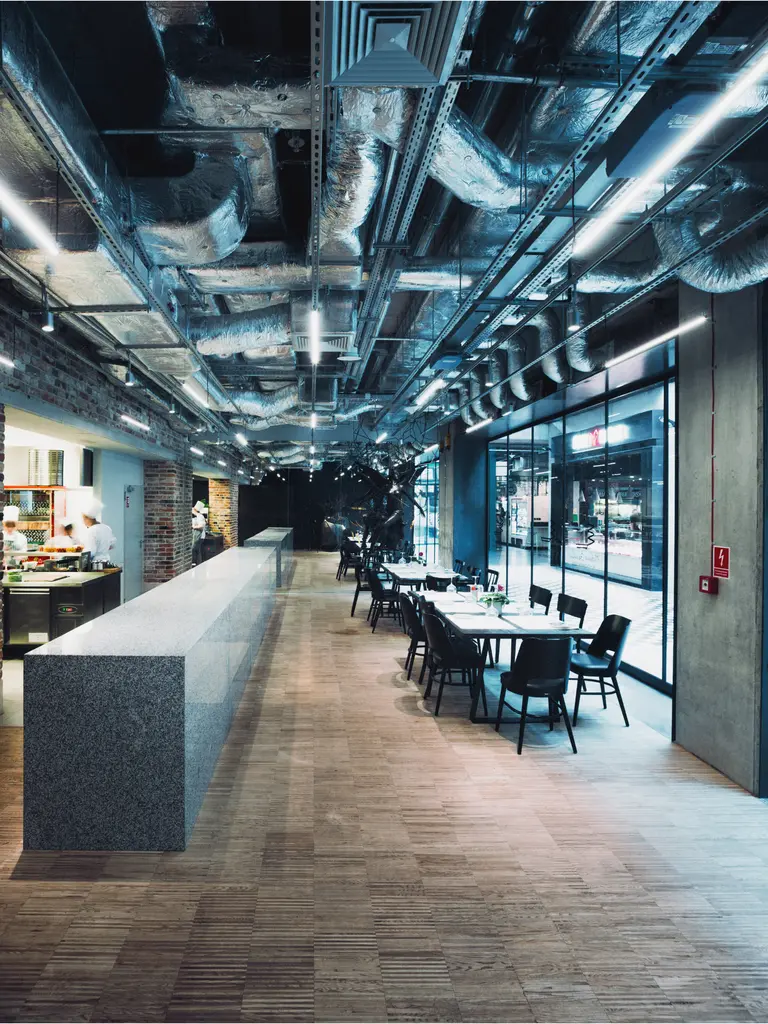 Wnętrze restauracji z industrialnym sufitem, minimalistycznym barem i skandynawskimi krzesłami.