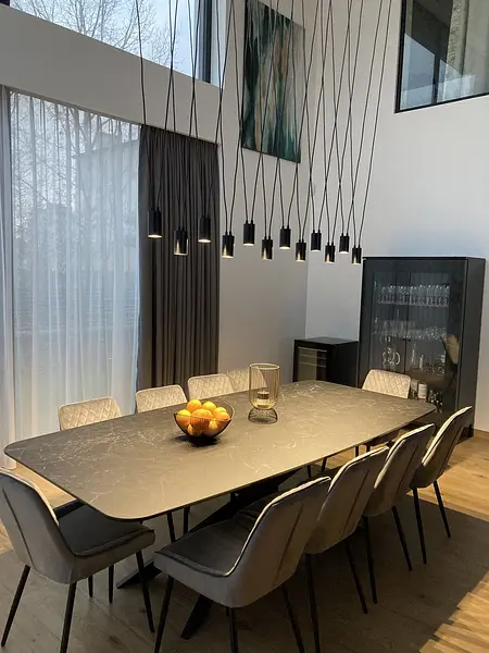 Jadalnia z dużym czarnym stołem, szarymi krzesłami i nowoczesnym oświetleniem.