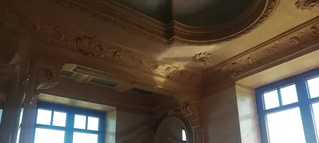 Wnętrze z ozdobnym sufitem i dużymi oknami, klasyczne detale architektoniczne.