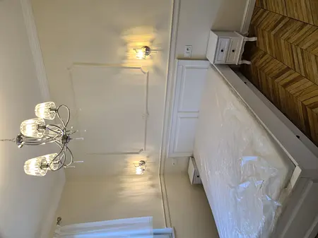 Tradycyjna sypialnia z białym łóżkiem, lustrami i eleganckim oświetleniem.