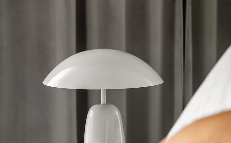 Sypialnia z białą lampą, szarymi zasłonami i pomarańczową poduszką. Współczesny design.