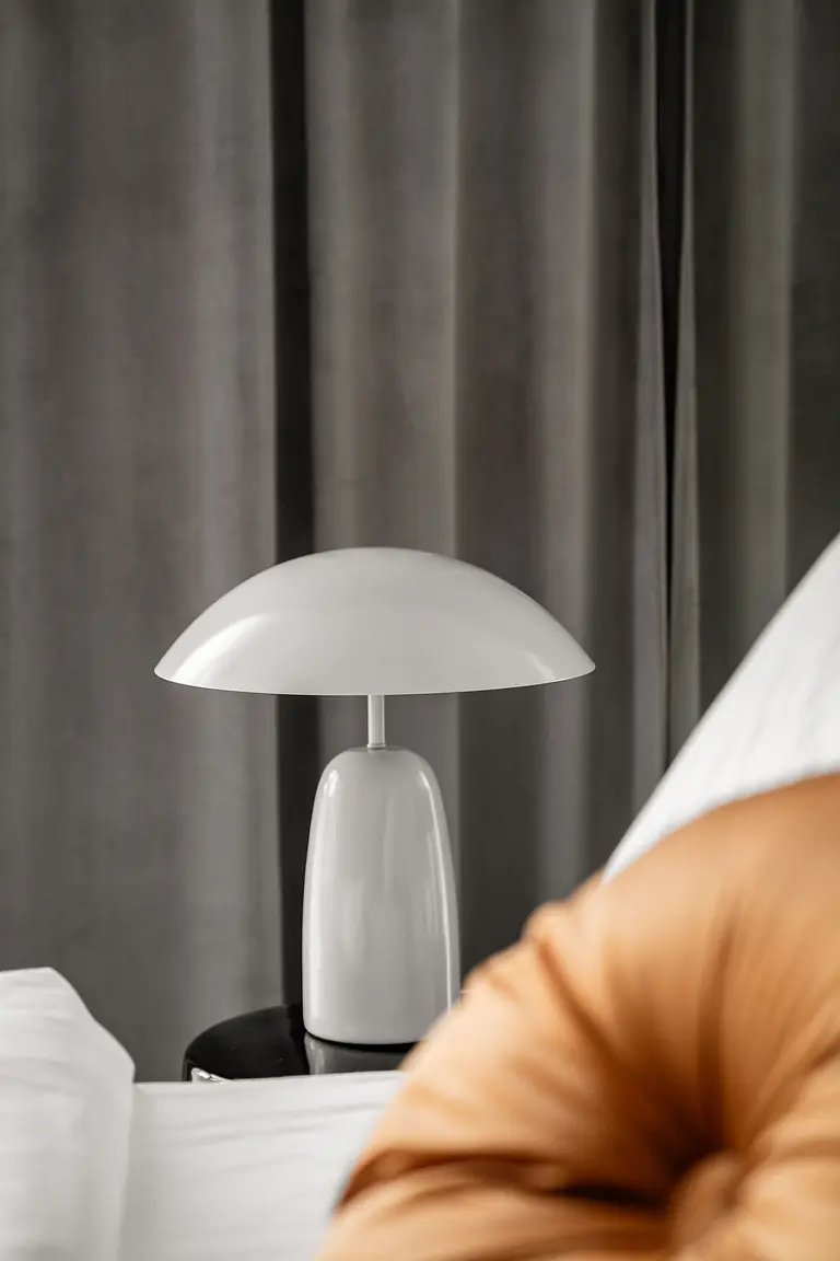 Sypialnia z białą lampą, szarymi zasłonami i pomarańczową poduszką. Współczesny design.