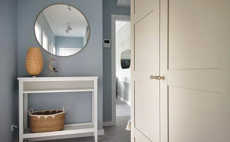 Przedpokój w stylu skandynawskim z białą komodą, okrągłym lustrem i dekoracjami.