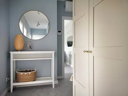 Przedpokój w stylu skandynawskim z białą komodą, okrągłym lustrem i dekoracjami.