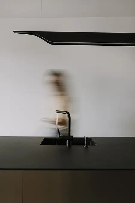 Wnętrze kuchni z czarnym blatem, minimalistycznym designem i nowoczesnym oświetleniem.