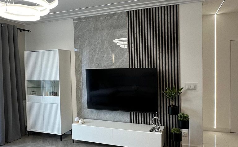Wnętrze salonu z minimalistycznym wystrojem, nowoczesnym telewizorem i szarym dywanem.