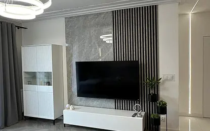 Wnętrze salonu z minimalistycznym wystrojem, nowoczesnym telewizorem i szarym dywanem.