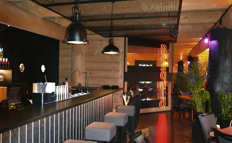 Wnętrze baru z industrialnym stylem, szarymi stołkami i drewnianymi akcentami.