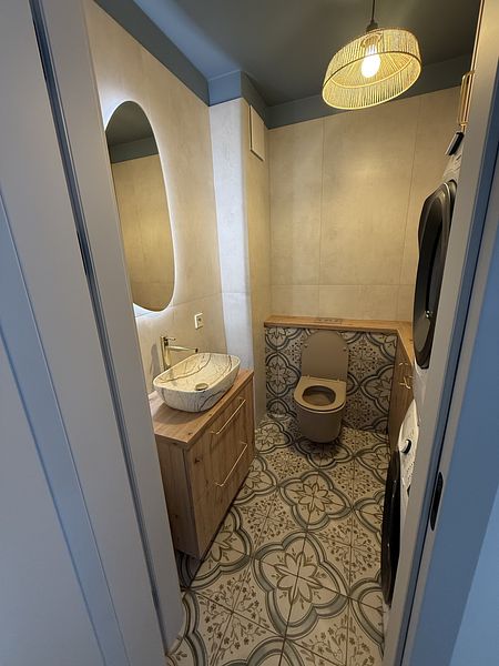 Nowoczesna łazienka w stylu boho z drewnianą szafką i dekoracyjną podłogą.