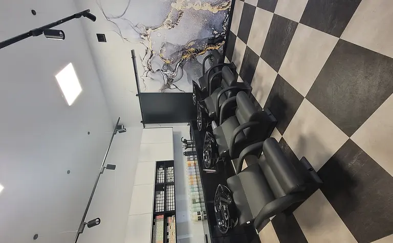 Salon fryzjerski z czarnymi fotelami i nowoczesnym wystrojem.