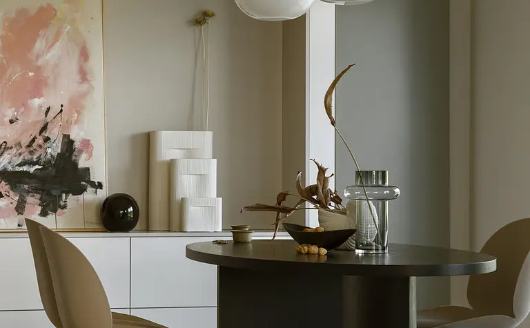 Wnętrze jadalni z okrągłym stołem, beżowymi krzesłami, minimalistycznymi akcentami.
