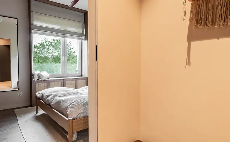 Przedpokój z drewnianą ławką, dużym lustrem oraz jasnymi ścianami. Styl boho, japandi i minimalistyczny.