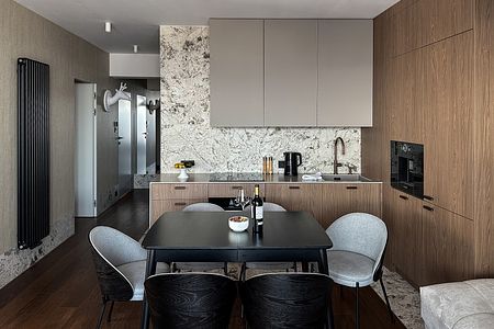 Wnętrze kuchni z drewnianymi meblami, marmurowym blatem i nowoczesnym oświetleniem.