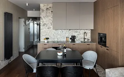 Wnętrze kuchni z drewnianymi meblami, marmurowym blatem i nowoczesnym oświetleniem.