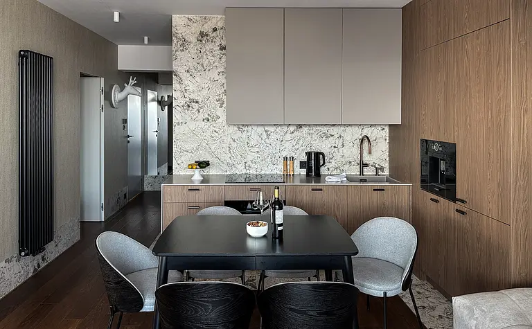 Wnętrze kuchni z drewnianymi meblami, marmurowym blatem i nowoczesnym oświetleniem.