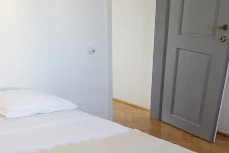 Wnętrze sypialni z białym łóżkiem, szarymi drzwiami i drewnianą podłogą, tradycyjny styl.