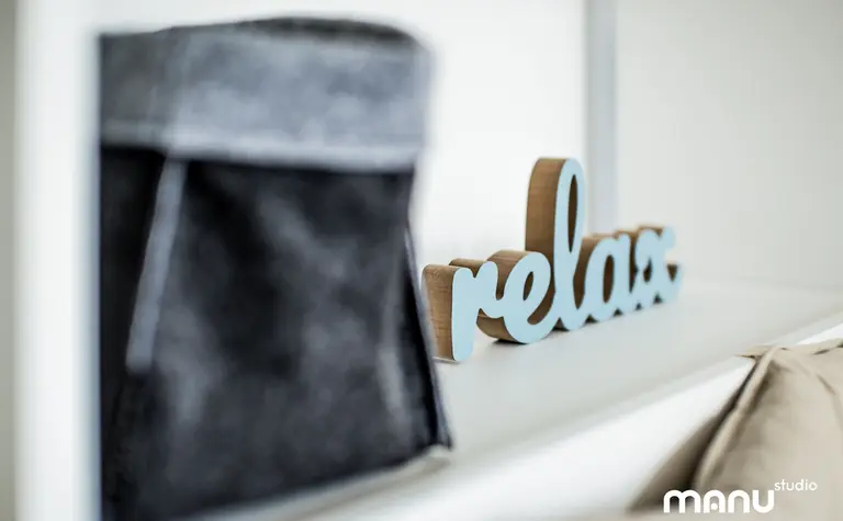 Nowoczesne wnętrze z minimalistycznym napisem relax oraz szarym pojemnikiem.