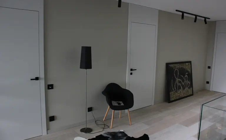 Minimalistyczne wnętrze z czarną lampą, białymi drzwiami i nowoczesnym wystrojem.