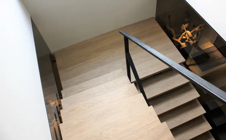 Widok schodów w minimalistycznym wnętrzu z drewnianymi stopniami i metalowym balustradą.