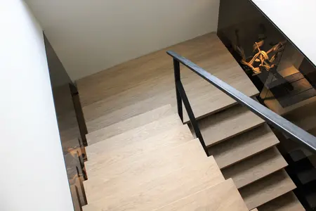 Widok schodów w minimalistycznym wnętrzu z drewnianymi stopniami i metalowym balustradą.
