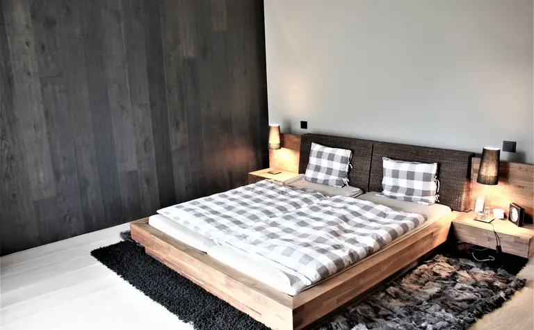 Minimalistyczna sypialnia z drewnianym łóżkiem, szarymi ścianami i nowoczesnym oświetleniem.