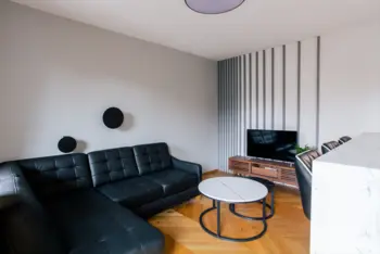 Wnętrze salonu z minimalistycznym wystrojem, czarna sofa, drewniane akcenty.