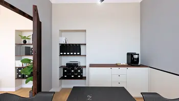 Wnętrze gabinetu z minimalistycznym biurkiem, nowoczesnym ekspresem do kawy i półkami.