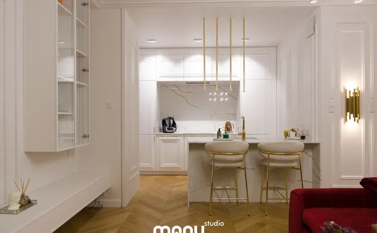 Wnętrze kuchni w stylu nowoczesnym z białymi meblami i złotymi detalami.