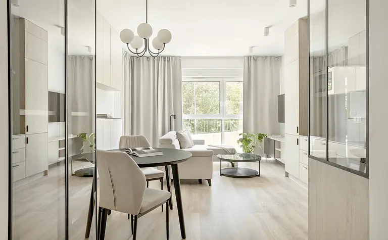 Wnętrze nowoczesnego salonu z minimalistycznym designem, jasnymi meblami i roślinnością.