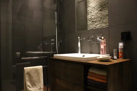 Nowoczesna łazienka z minimalistycznym designem, szarymi ścianami i drewnianymi akcentami.