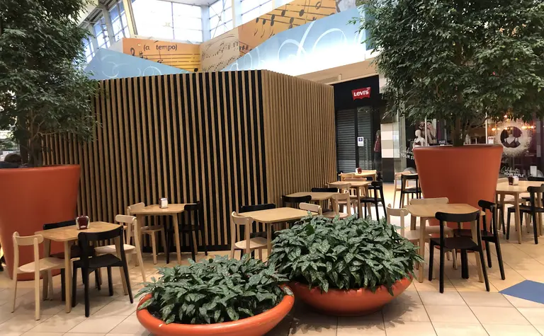 Wnętrze kawiarni z drewnianymi stołami i dużymi roślinami. Styl japandi, minimalistyczny, nowoczesny.
