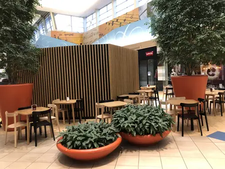 Wnętrze kawiarni z drewnianymi stołami i dużymi roślinami. Styl japandi, minimalistyczny, nowoczesny.