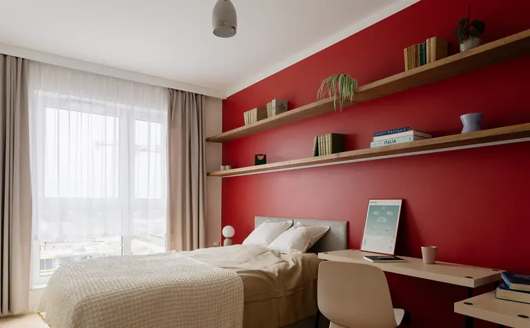 Sypialnia w stylu minimalistycznym z czerwoną ścianą, drewnianymi półkami i nowoczesnym biurkiem.