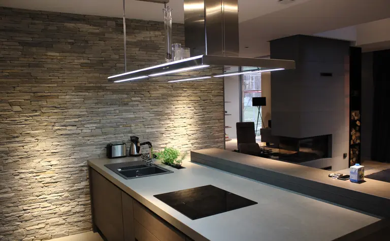 Wnętrze kuchni z minimalistycznym designem, kamienną ścianą i nowoczesnymi akcesoriami.