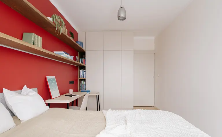 Sypialnia minimalistyczna z czerwoną ścianą, drewnianymi półkami i nowoczesnym biurkiem.
