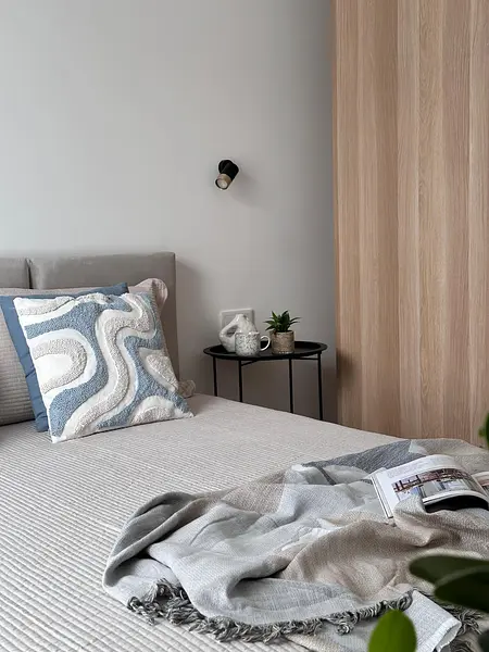 Współczesna sypialnia z szarym wezgłowiem, poduszkami i drewnianą szafą.
