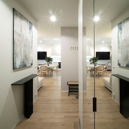 Nowoczesny przedpokój z drewnianą podłogą, jasnymi ścianami i obrazami w stylu quiet luxury.