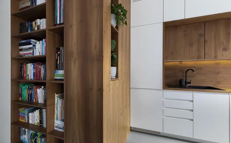 Minimalistyczne wnętrze kuchni z drewnianą półką i nowoczesnymi białymi meblami.