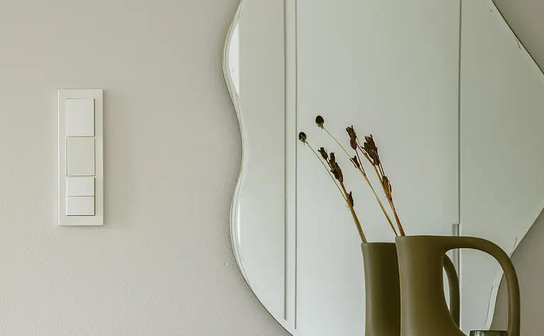 Minimalistyczne wnętrze z okrągłym lustrem i dekoracjami w stylu quiet luxury.