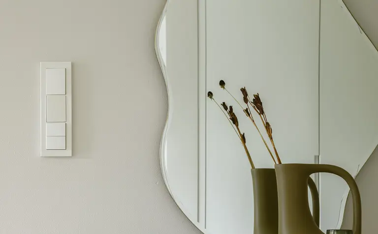 Minimalistyczne wnętrze z okrągłym lustrem i dekoracjami w stylu quiet luxury.
