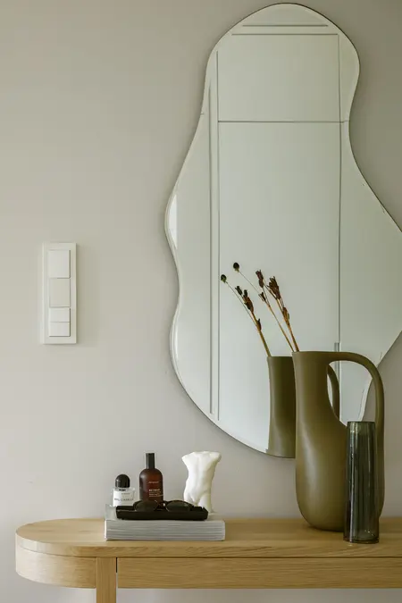 Minimalistyczne wnętrze z okrągłym lustrem i dekoracjami w stylu quiet luxury.