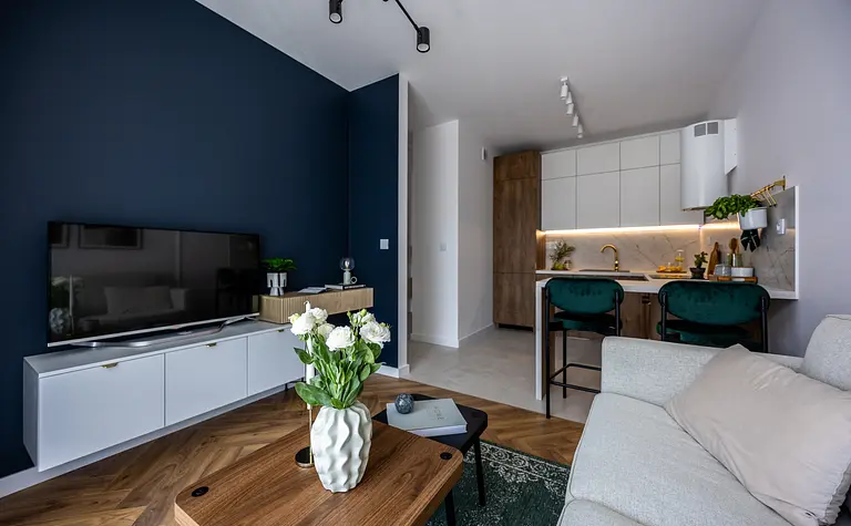 Nowoczesny salon z białymi meblami i drewnianymi detalami, zieloną roślinnością.