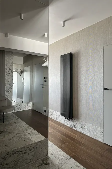 Przedpokój z nowoczesnymi lustrami i czarnym grzejnikiem na tle jasnych ścian.